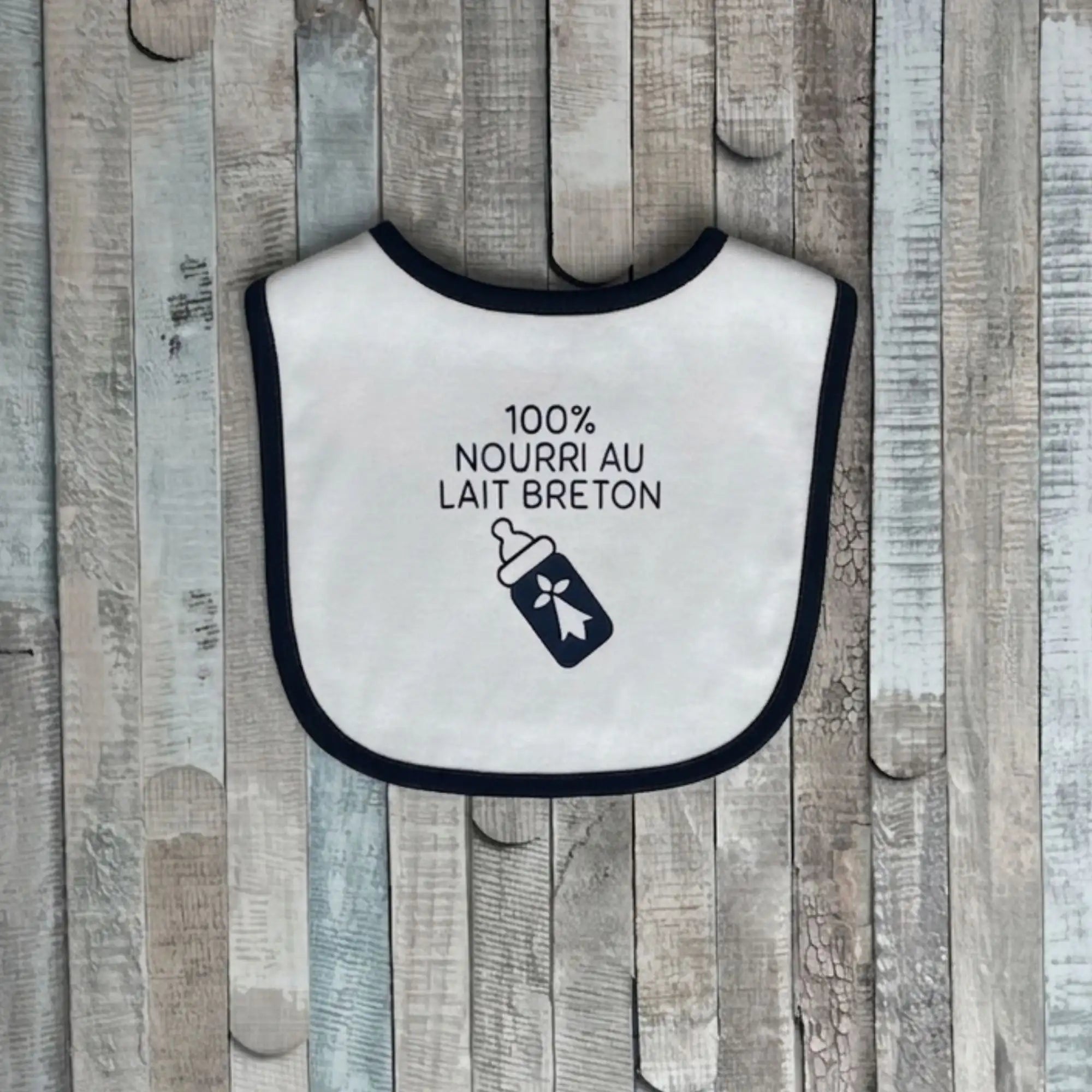 Bavoir bébé blanc bordure noire avec inscription 100% Nourri au Lait Breton et illustration de biberon à hermine bretonne.