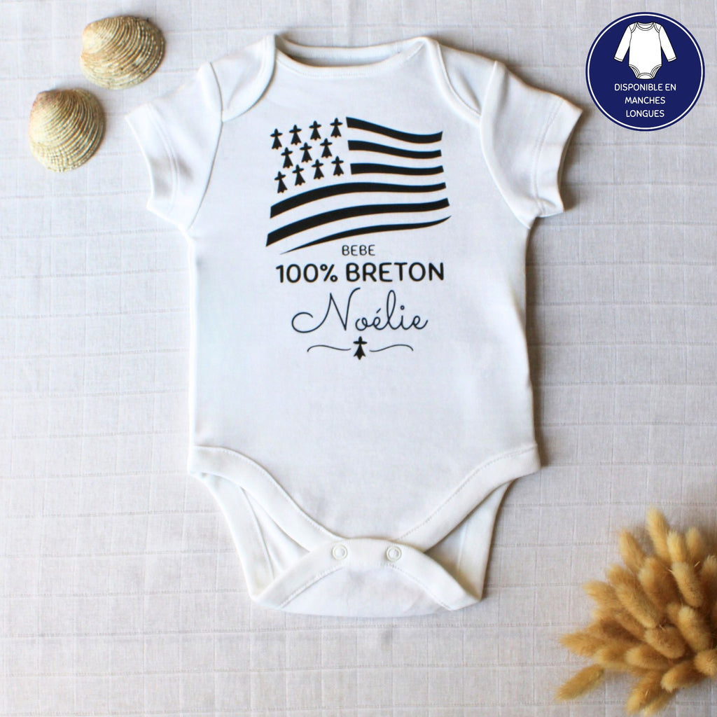 Body blanc pour bébé en coton personnalisé avec le prénom Noélie et le drapeau breton Gwenn ha du, posé à plat avec des coquillages.