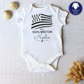 Body blanc pour bébé en coton personnalisé avec le prénom Noélie et le drapeau breton Gwenn ha du, posé à plat avec des coquillages.