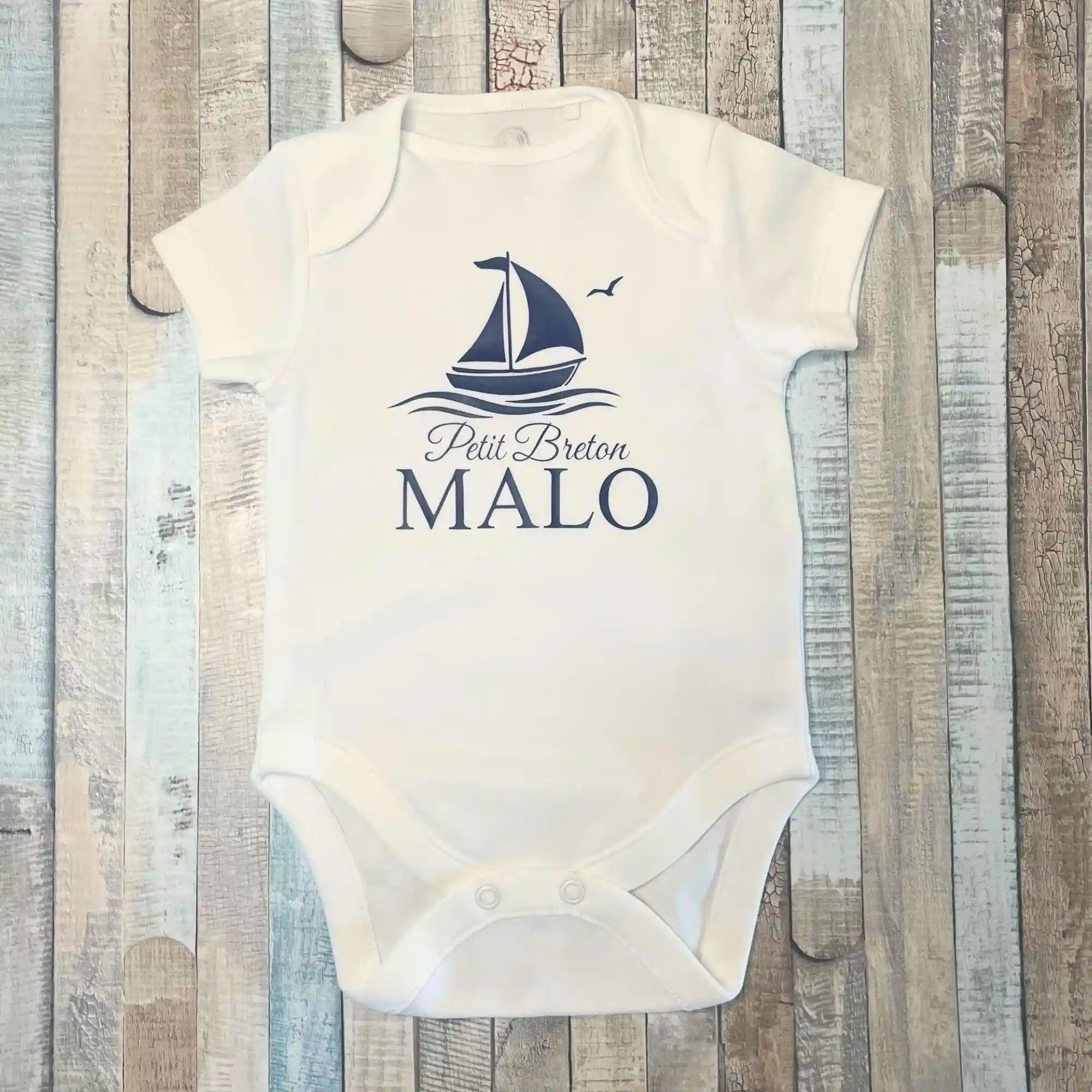 Body blanc à manches courtes pour bébé garçon, personnalisé avec le prénom Malo, l'inscription Petit Breton, un bateau à voile, le tout en bleu marine.  DIsponible en manches longues