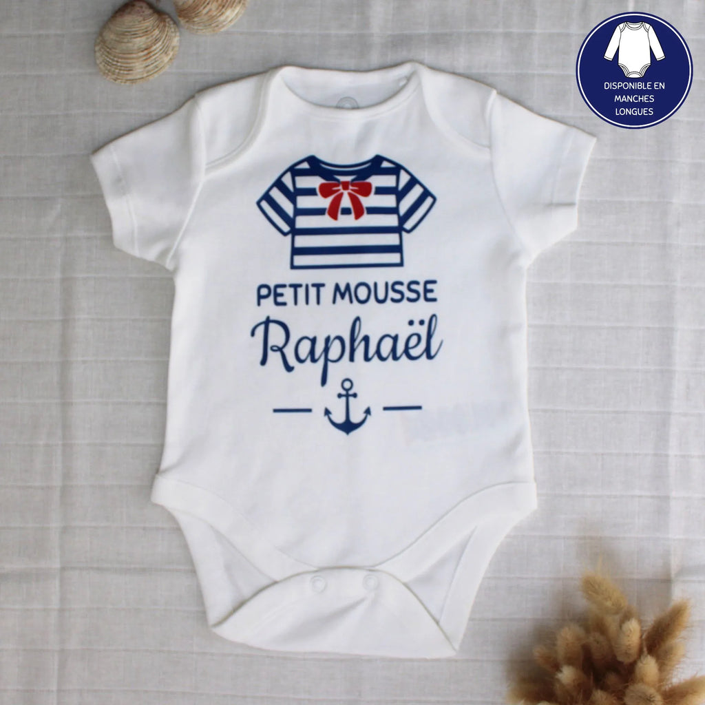 Body blanc pour bébé en coton personnalisé avec le prénom personnalisé et l'inscription petit mousse, et une marinière à noeud rouge, posé à plat avec des coquillages.