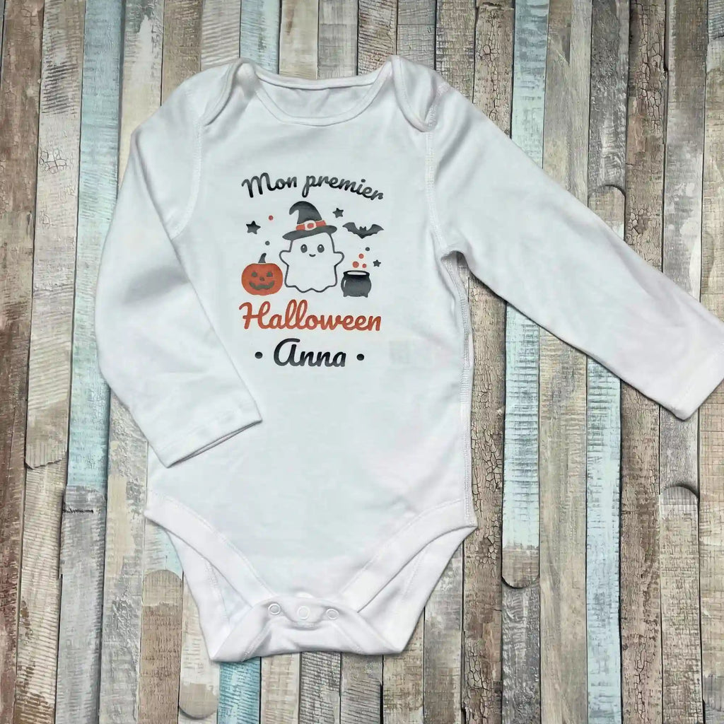 Body bébé personnalisé blanc "Mon premier Halloween Anna" avec motifs fantôme, citrouille et chaudron sur fond bois.