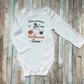 Body bébé personnalisé blanc "Mon premier Halloween Anna" avec motifs fantôme, citrouille et chaudron sur fond bois.