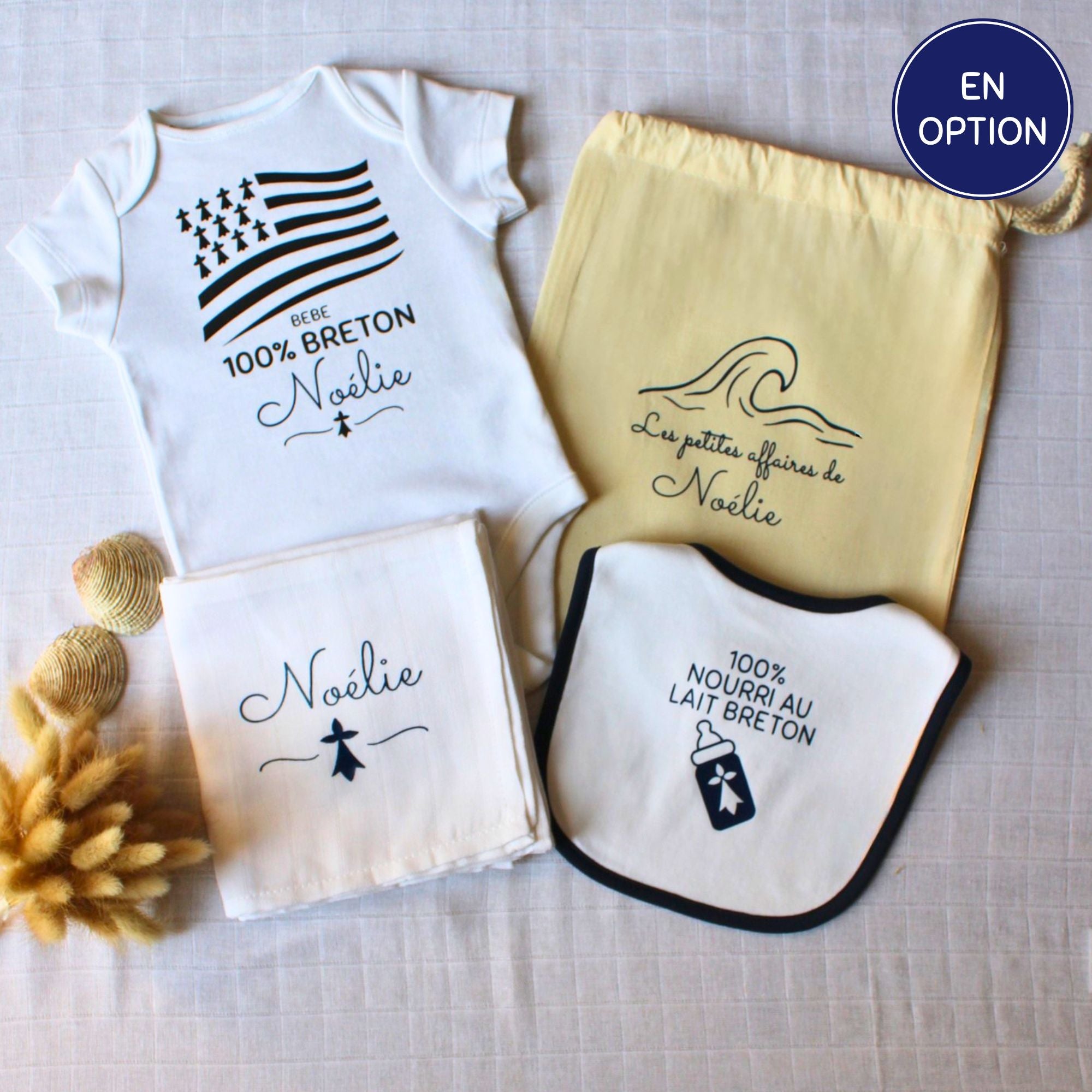 Kit de naissance breton personnalisé comprenant un body blanc 100% breton, un bavoir nourri au lait breton, un lange blanc et un pochon de rangement en tissu jaune.