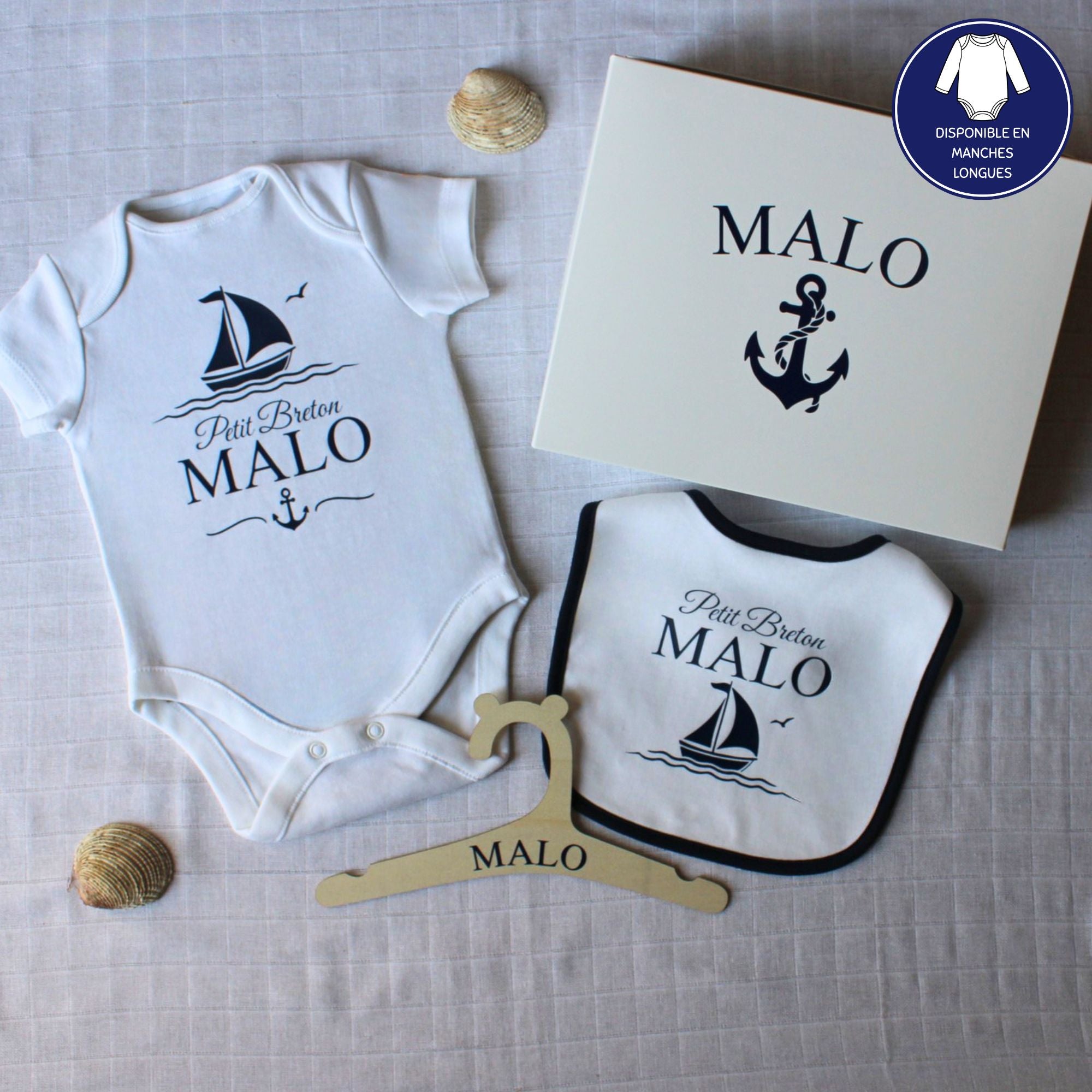 Un coffret cadeau de naissance personnalisé pour garçon prénom Malo. Le kit comprend un body, un bavoir à liseré bleu marine, un cintre en bois et une boîte cadeau, tous décorés d'un motif de bateau marine.