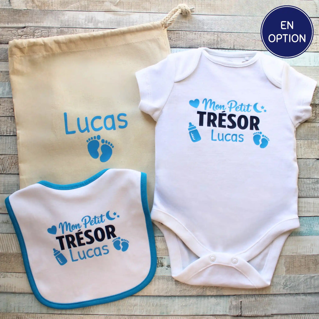 Présentation d'une parure de naissance "Lucas" : un body, un bavoir et un sac cadeau en coton naturel, tous personnalisés et disposés ensemble sur bois gris