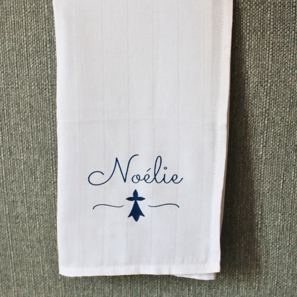 Lange en coton blanc pour bébé personnalisé avec le prénom Noélie écrit en bleu marine au-dessus d'un symbole d'hermine bretonne.