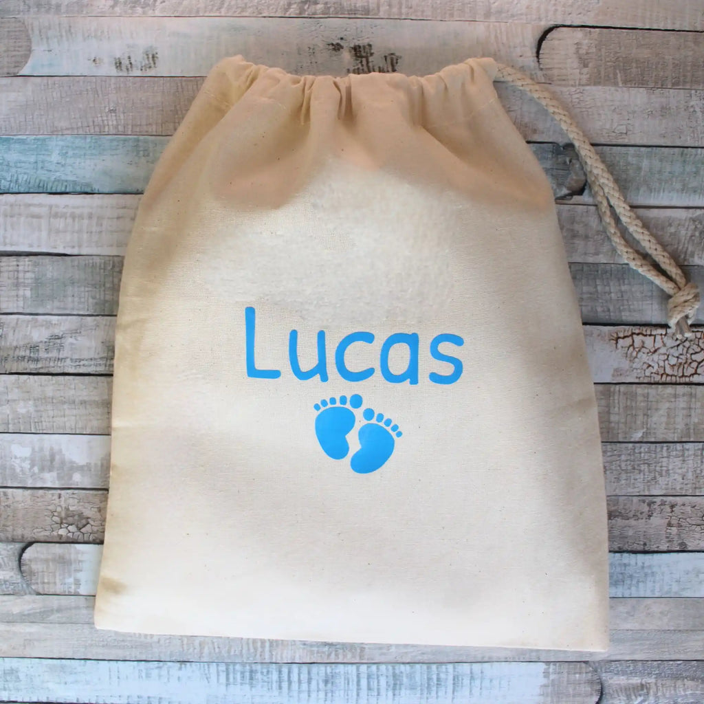 Pochon de rangement en tissu beige personnalisé pour bébé avec le prénom Lucas et des petites empreintes de pieds bleues